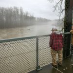 Two men look out over the confluence of the North and South forks of the Stillaguamish River from atop Haller Bridge during heavy flooding on Tuesday, Dec. 5, 2023, in Arlington, Washington. People from all over the area came to the bridge to get a look at the river. (Ryan Berry / The Herald)