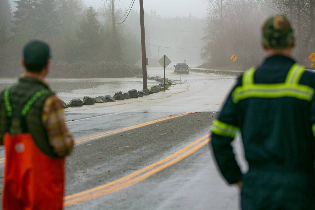 Two drivers watch as a person in a lifted Ford fords a flooded Highway 530 near Twin Rivers Park during heavy flooding on Tuesday, Dec. 5, 2023, in Arlington, Washington. (Ryan Berry / The Herald)