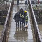 District 4 firefighters walk a man and his dog across a bridge to be checked out by medics after being rescued from a flooded portion of Al Borlin Park on Tuesday, Dec. 5, 2023 in Monroe, Washington. (Olivia Vanni / The Herald)