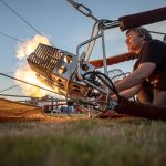 Erin Romaneschi, 33, fires up the burner and injects a hot air balloon with flame to heat the air inside during Kla Ha Ya Days at Harvey Field in Snohomish, Washington on Friday, July 14, 2023. (Annie Barker / The Herald)