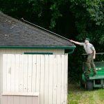 Park Ranger assistant Aidan Link does his best to remove debris from the top of the restroom at Kayak Point Regional County Park on Friday, June 14, 2024, near Stanwood, Washington. Link said park staff are still working to tidy up the park as they prepare for the busy season. (Ryan Berry / The Herald)