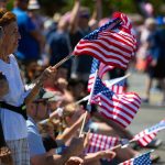 Members of the crowd wave flags during Everett’s Fourth of July Parade on Thursday, July 4, 2024, in downtown Everett, Washington. (Ryan Berry / The Herald)