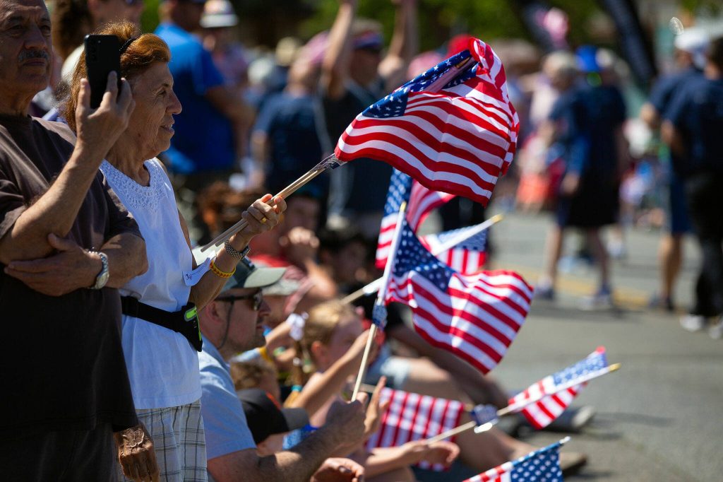 Members of the crowd wave flags during Everetts Fourth of July Parade on Thursday, July 4, 2024, in downtown Everett, Washington. (Ryan Berry / The Herald)
