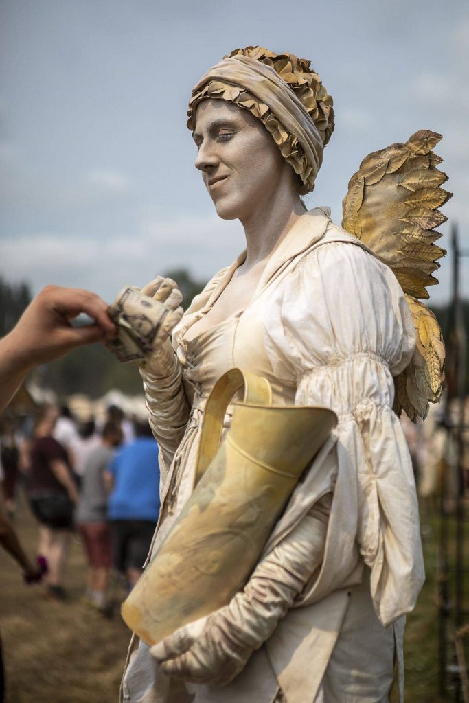Faye, the living statue, accepts tips in their pitcher during the Washington Midsummer Renaissance Faire at Sky Meadows Park in Snohomish, Washington on Sunday, Aug. 6, 2023. (Annie Barker / The Herald)