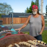 Tlingit artist Fred Fulmer stands over one of his completed totem poles while speaking about it on Wednesday, May 8, 2024, in the back yard of his home in Everett, Washington. (Ryan Berry / The Herald)