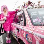 Marty Vale, a car artist, stands next to her hot pink and trinket-covered 1991 Toyota Corolla that draws attention wherever she goes. Vale, 76, of Lynnwood, also joins other cartists at parades and art shows. This is her third art car. (Olivia Vanni / The Herald)
