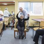 Lorne Dalgleish pushes Mary Ann Karber in a rolling chair over to the wheel as she celebrates with her legs up after having her name drawn to spin during Wheel of Fortune at Washington Oakes in Everett. (Olivia Vanni / The Herald)