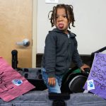 Zakai Richie, 3, who attends the Early Learning Center, sits in a cart with signs protesting the centers closure on Tuesday, May 20, 2025 in Everett, Washington. (Will Geschke / The Herald)