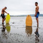 Ellis Johnson, 16, left, and brother Garrett Johnson, 13, take a breather after trying to find enough water to skim board on without sinking into the sand during opening day of Jetty Island on Friday, July 5, 2019 in Everett, Wash. (Olivia Vanni / The Herald)