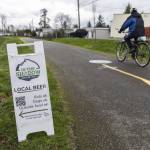 A person bikes past an In The Shadow Brewing sign along the Centennial Trail on Wednesday, March 12, 2025 in Arlington, Washington. (Olivia Vanni / The Herald)