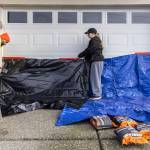 Bella Reid, right, and her fiancé Hector Rodrigues cover their garage door with tarps and water activated flood bags in preparation for potential flooding on Tuesday, Dec. 9, 2025 in Snohomish, Washington. (Olivia Vanni / The Herald)