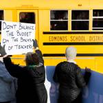 Melody Schneider holds a sign protesting pay cuts to teachers as an Edmonds School District bus passes by during an Edmonds College faculty union rally as part of a national day of action outside of the Lynnwood Event Center on Tuesday, March 4, 2025, in Lynnwood, Washington. (Olivia Vanni / The Herald)