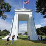People walk adjacent to the border with Canada at the Peace Arch in Peace Arch Historical State Park, where cars behind wait to enter Canada at the border crossing Monday, Aug. 9, 2021, in Blaine, Wash.