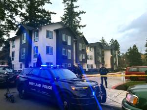 Portland police officers stand behind police tape in front of an apartment building in east Portland. (Photo by Alex Baumhardt/Oregon Capital Chronicle)
