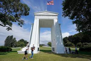 People walk adjacent to the border with Canada at the Peace Arch in Peace Arch Historical State Park, where cars behind wait to enter Canada at the border crossing Monday, Aug. 9, 2021, in Blaine, Wash. Canada lifted its prohibition on Americans crossing the border to shop, vacation or visit, but America kept similar restrictions in place, part of a bumpy return to normalcy from coronavirus travel bans. (AP Photo/Elaine Thompson)