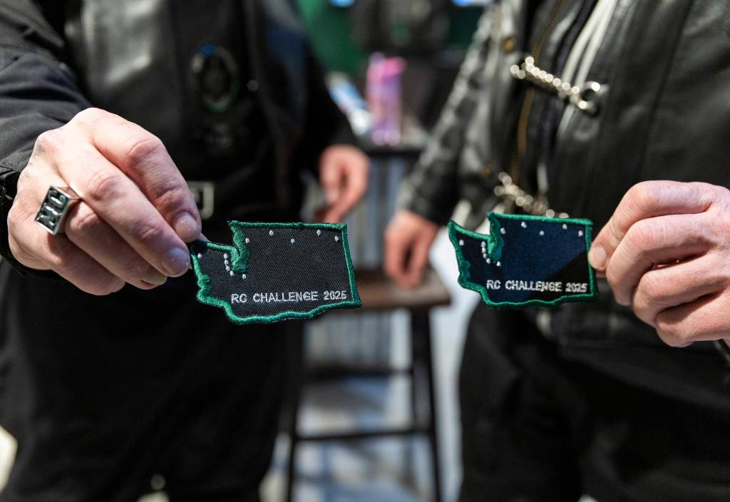Two members show off their ride patches they earned on March 12, 2026, in Everett. (Olivia Vanni / The Herald)