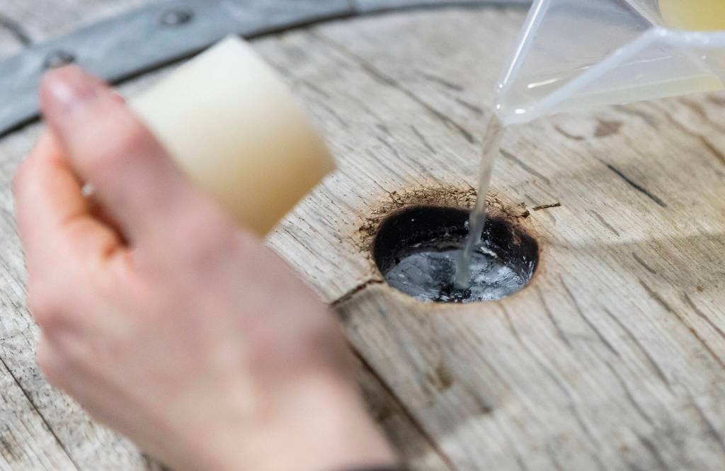 Katie Cochrane pours cider into a barrel to top it off at Garden Path Fermentation on Wednesday, Jan. 7, 2026 in Burlington, Washington. (Olivia Vanni / The Herald)