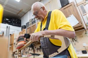 John Ellis sands the side of a dulcimers frame in preparation for a small repair in his workshop on Thursday, May 7, 2026 in Arlington, Washington. (Olivia Vanni / The Herald)